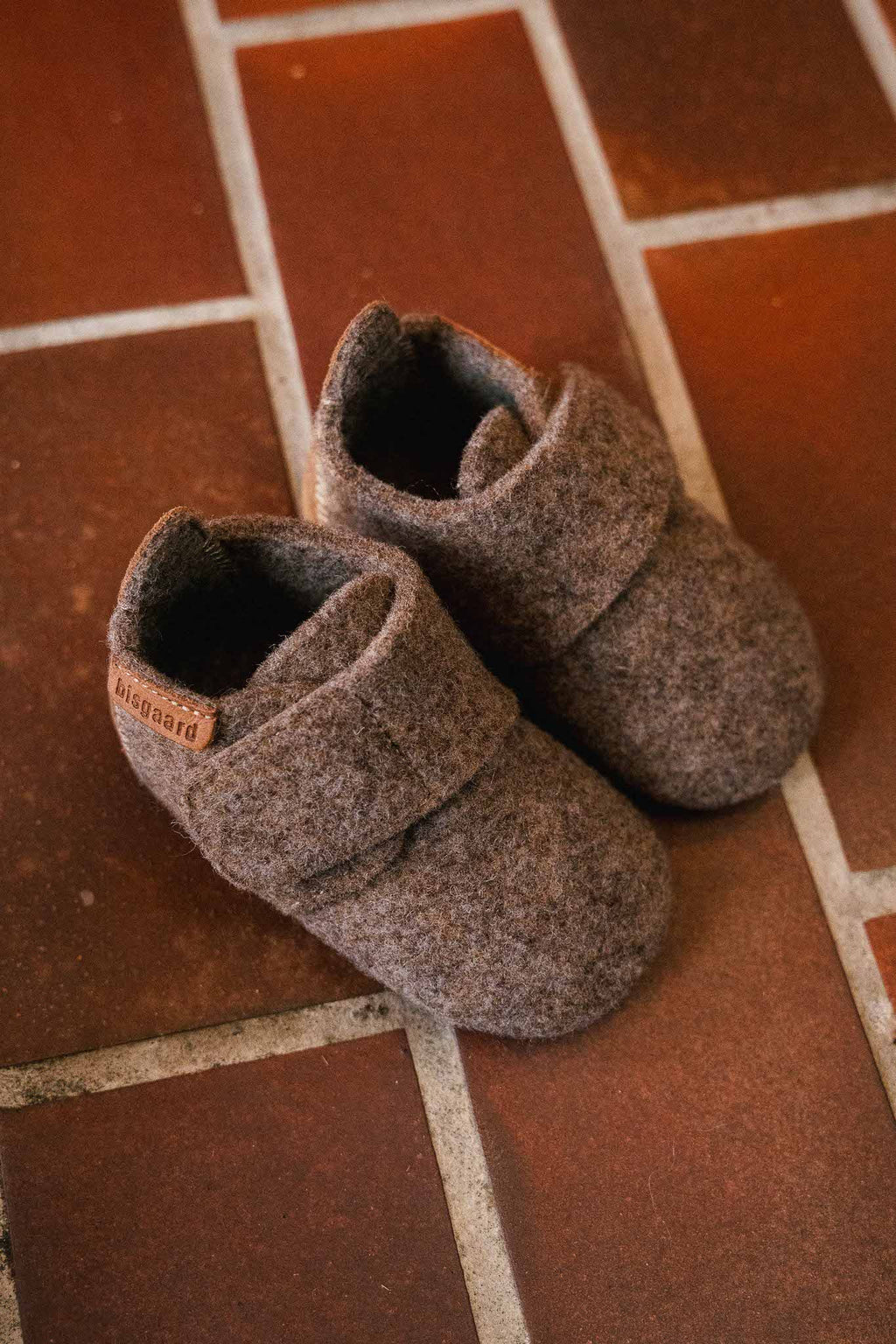Baby Wool Camel – Chaussons bébé en laine – Bisgaard : deux chaussons sur un sol carrelé.
