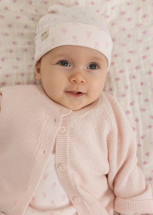 Strampler mit Füßchen – Rubetta Mini Bloom – MarMar Copenhagen: Baby trägt die hellrosa Babymütze in einem Wickelkorb.