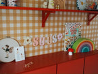 Ochre Yellow Gingham wallpaper by Atelier Chien with a red wall shelf and cabinet, close-up.
