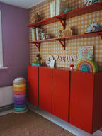 Ochre Yellow Gingham wallpaper by Atelier Chien behind a red cabinet and wall shelves.