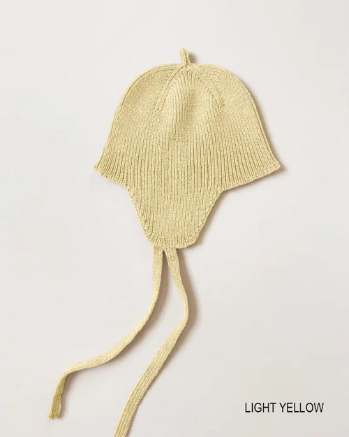 Bonnet Kota – Baby mutsje met oorkleppen – HVID: babymuts met oorkleppen en strikbandjes, liggend gefotografeerd.