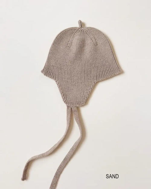 Bonnet Kota – Baby mutsje met oorkleppen – HVID: babymuts met oorkleppen en strikbandjes, liggend gefotografeerd.