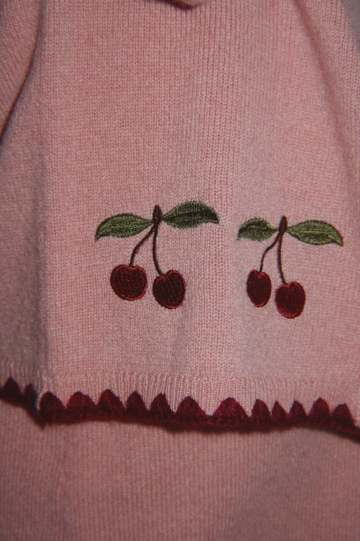 Wollen vest Collette – Pale Blush – Konges Sløjd: detail van de geborduurde kersen en onderrand van het roze vest.
